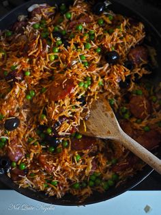 a skillet filled with rice, peas and meats next to a wooden spoon