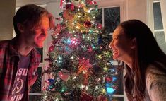 a man and woman standing in front of a christmas tree with their mouths open while looking at each other