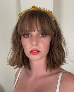 a woman with freckled hair wearing a gold headband and white bra top