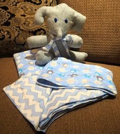 an elephant stuffed animal sitting on top of a blue and white blanket next to pillows