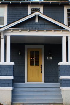 a blue house with a yellow door and white trim on the front porch is shown