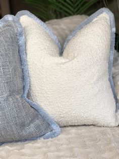 two blue and white pillows sitting on top of a bed next to a potted plant