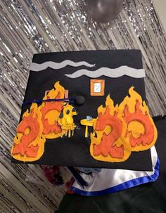 a graduation cap decorated with fire and flames on it's side, sitting in front of a backdrop