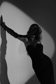 a woman in a black dress is holding her arm out to the side and casting a long shadow