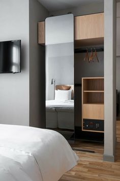 a bedroom with a bed, mirror and television mounted on the wall next to it