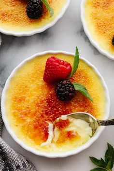 three small white bowls filled with pudding and raspberries on top of a marble table