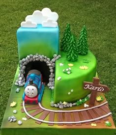 a thomas the train birthday cake on top of a green field with trees and rocks