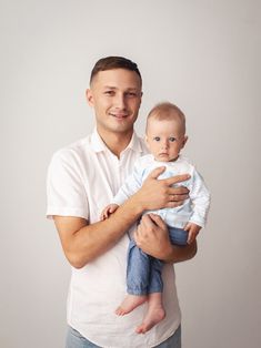 a man holding a baby in his arms and smiling at the camera while wearing a white shirt