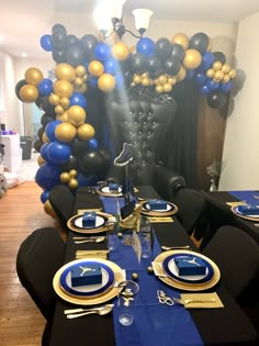 the table is set with blue and gold plates, silverware, and black napkins