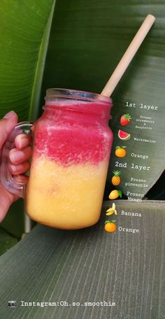 a hand holding a mason jar filled with orange and raspberry smoothie next to a banana leaf