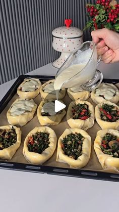 a person pours milk into small pastries on a baking tray with flowers in the background