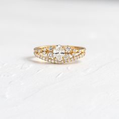 a yellow gold ring with two rows of diamonds on the band and an oval shaped center stone