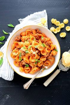 a bowl filled with pasta and meat on top of a wooden table next to bread