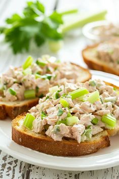 two pieces of bread with chicken salad on them sitting on a white plate next to parsley