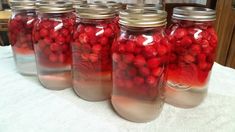 four jars filled with red berries sitting on top of a table