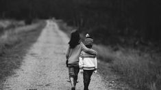 two children walking down a dirt road in black and white, one holding the other's hand