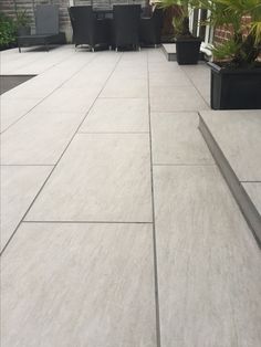 an outdoor patio with potted plants on the side and black chairs in the back