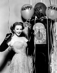 a black and white photo of a woman in a dress next to a clock with happy new year balloons