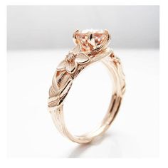 a rose gold engagement ring with an oval shaped center stone and leaves on the band