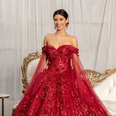 a woman in a red gown standing on a couch with her hands behind her back