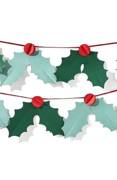 two green and red paper holly decorations hanging from clothes pins on a white background with clippings