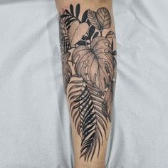 a black and white tattoo on the leg of a woman's arm with leaves