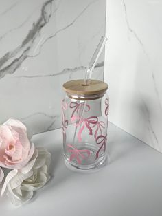 a pink flower sitting next to a glass jar with a straw in it on a table