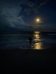 a person standing on the beach at night with the moon in the sky above them