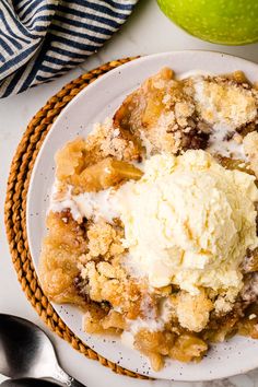 a white plate topped with an ice cream covered crumbled apple cobbler next to a green apple