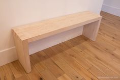 a wooden bench sitting on top of a hard wood floor next to a white wall