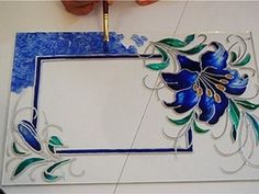 a hand holding a paintbrush over a blue and white tile with flowers on it