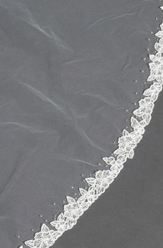 the edge of a wedding veil with white flowers on grey fabric, as seen from above