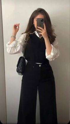 a woman taking a selfie in front of a mirror wearing black overalls and white shirt