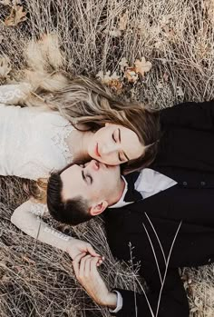 a man and woman laying on the ground in tall grass with their heads touching each other