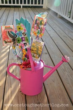 a pink watering can filled with cards and flowers on a wooden deck next to a white picket fence