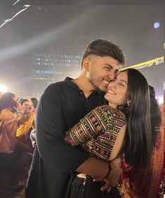 a man and woman hugging each other in front of a crowd at an event with lights on