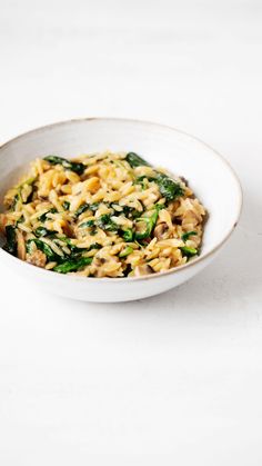 a white bowl filled with pasta and spinach