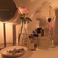 an assortment of perfumes on a table next to a vase with a rose in it