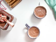 two mugs filled with hot chocolate on top of a white table next to a green towel