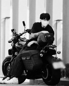 black and white photograph of a man sitting on a parked motorcycle with his arm wrapped around the seat