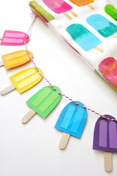 popsicle garland made out of popsicles on a white table with colorful paper and string