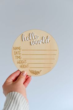 a person holding up a wooden sign with the words hello world written on it in gold lettering