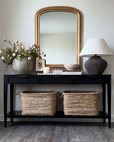 a console table with two baskets and a large mirror on the wall in front of it