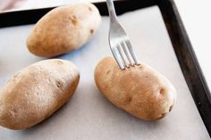 two potatoes on a baking sheet with a fork stuck in them