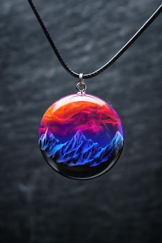 a glass pendant is hanging on a black cord and has mountains in the background with red, blue, and purple colors