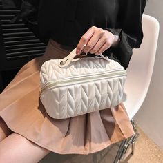 a woman sitting on a chair holding a white bag with zippers and handles in front of her