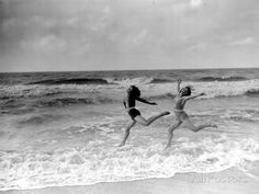 two women jumping into the air on top of a sandy beach next to the ocean