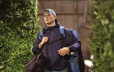 a man with a backpack is walking down the street in front of some bushes and trees