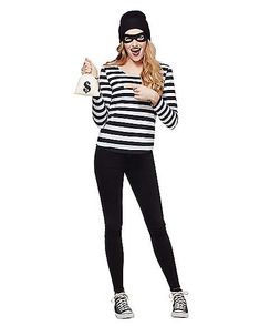 a woman in black and white striped shirt holding up a cat mask while standing on one leg