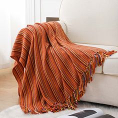 an orange striped blanket sitting on top of a white couch next to a remote control